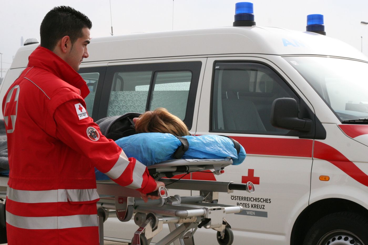 Ein Zivildiener in Uniform des Österreichischen Roten Kreuzes im Rettungs- und Krankentransportdienst, im Hintergrund ist ein Rettungsfahrzeug